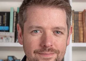 Portrait of children’s author Alastair Chisholm in front of bookshelves