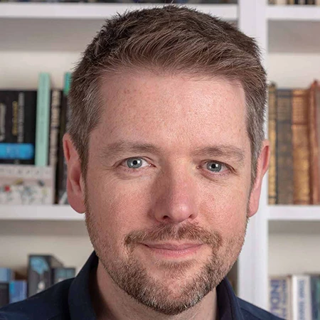 Portrait of children’s author Alastair Chisholm in front of bookshelves