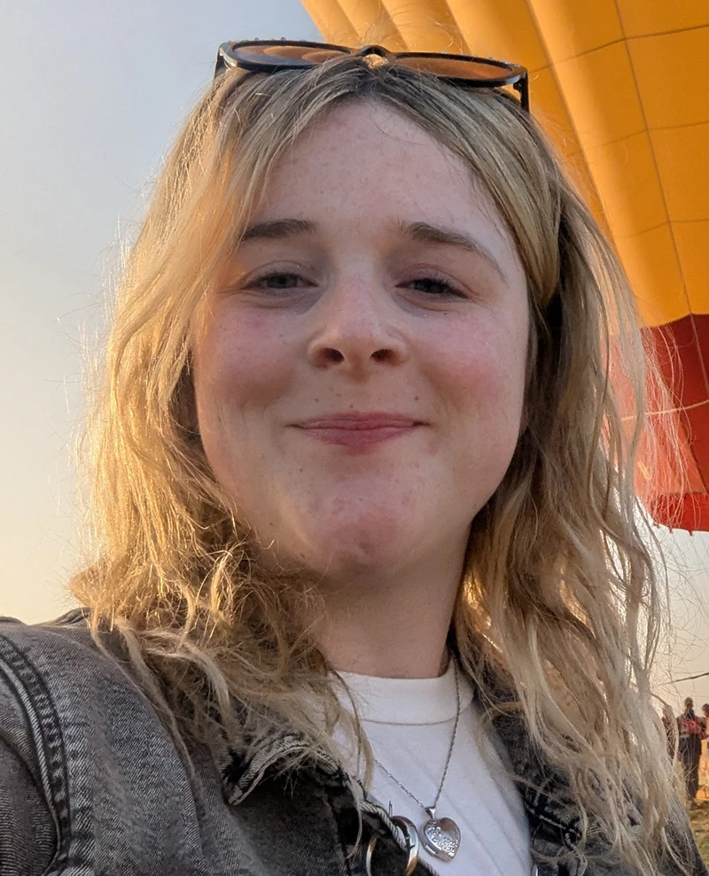 Emma Kames smiling outdoors in front of a large yellow structure.