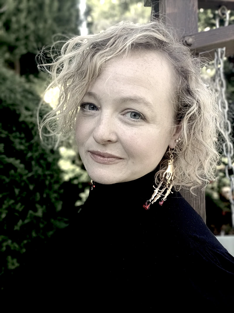 Portrait of Lucy Ribchester outdoors, wearing a dark top and looking towards the camera.