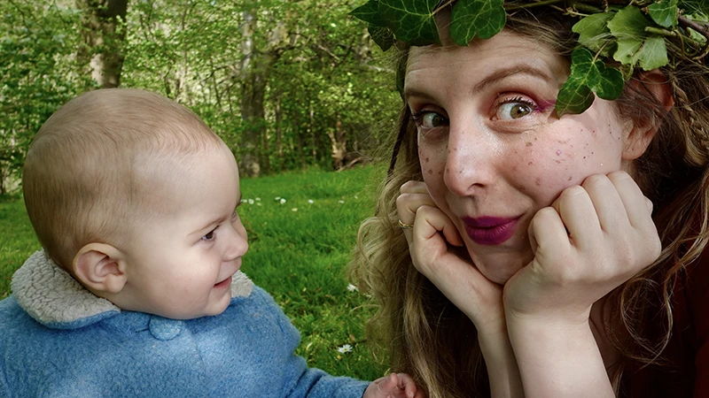 Performer wearing ivy leaves and face paint interacting with a baby during the Heebie Jeebies performance.
