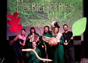 Performers posing on stage with oversized leaf props and insect puppets from the children's show Heebie Jeebies.
