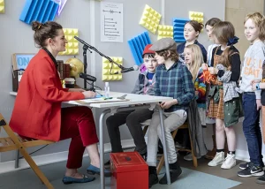 Performer interviewing a young child at a microphone in the colourful Experts Radio Lab studio.